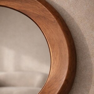 May include: A circular wall mirror featuring a thick, smooth, medium-brown wooden frame with a visible natural grain pattern. The frame has a rounded, curved profile that creates a soft, continuous edge around the reflective glass surface.