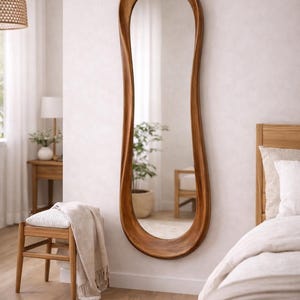 May include: A full-length wall mirror featuring a thick, organic, wavy wooden frame with a warm brown finish. The mirror has an elongated, irregular oval shape that tapers and curves along the sides, creating a fluid, non-symmetrical silhouette.