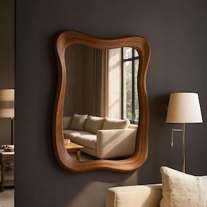 May include: A wall-mounted mirror featuring a thick, wavy, brown wooden frame with a visible grain pattern. The mirror has a smooth, reflective surface that displays a reflection of a living room interior with a beige sofa and a window.