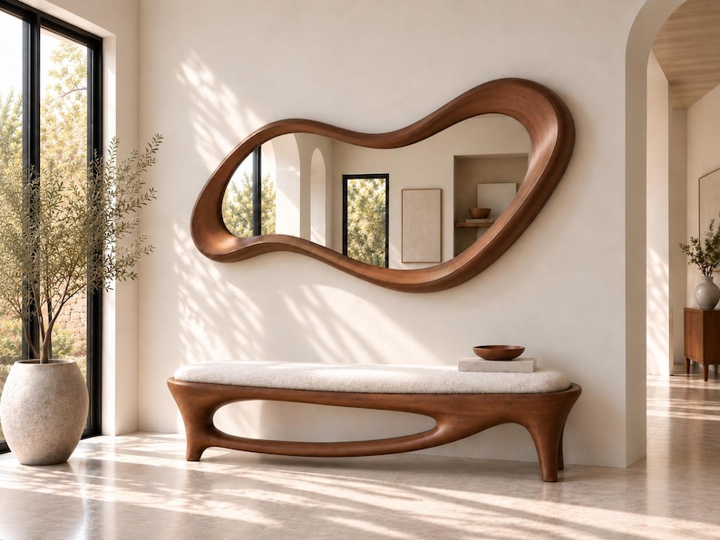 May include: A wall-mounted mirror with an irregular, organic wooden frame featuring a smooth, curved shape. Below it sits a matching wooden bench with a cream-coloured upholstered seat, supported by a continuous, fluid base design.
