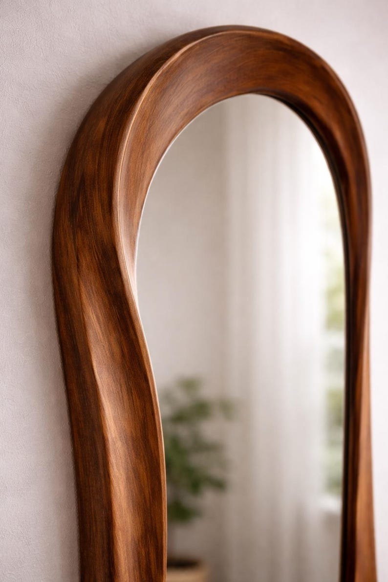 May include: A wall mirror featuring a tall, arched frame crafted from dark brown wood with a visible grain pattern. The frame has a smooth, undulating, and curved silhouette that creates a fluid, organic shape around the reflective glass surface.