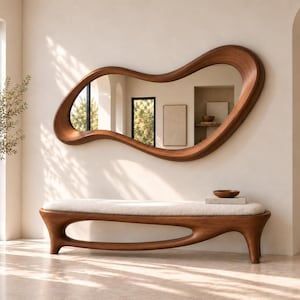 May include: A large, organic-shaped wall mirror with a smooth, dark wood frame featuring fluid, asymmetrical curves. Below it sits a matching wooden bench with a long, cream-coloured upholstered seat and a sculptural, open-base frame design.