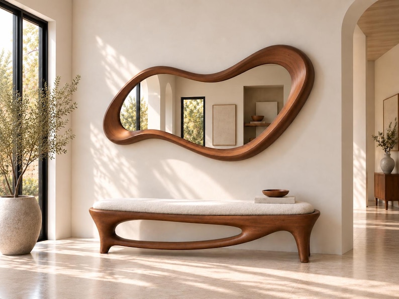 May include: A large, organic-shaped wall mirror with a smooth, dark wood frame featuring fluid, asymmetrical curves. Below it sits a matching wooden bench with a long, cream-coloured upholstered seat and a sculptural, open-base frame design.