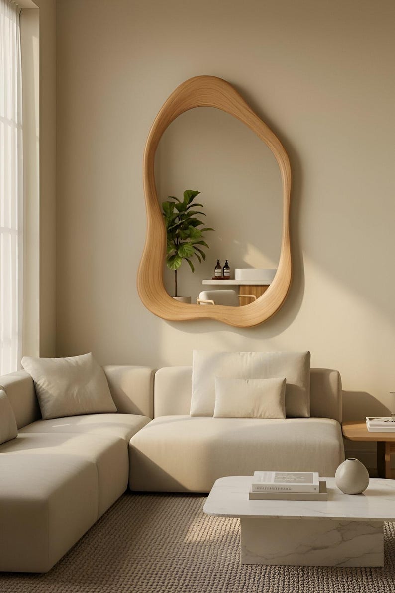 Puede incluir: Un espejo de pared con un marco de madera irregular, org&aacute;nico y ondulado con un acabado de veta de madera natural clara. El espejo refleja una planta verde en maceta, un estante blanco y dos botellas peque&ntilde;as, mostrando una silueta curva.