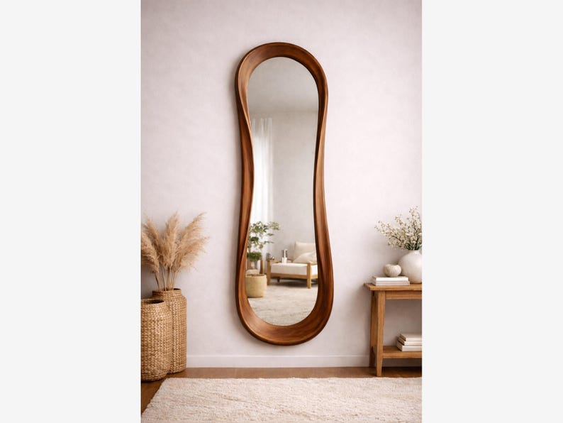May include: A full-length wall mirror featuring a smooth, organic, wavy wooden frame with a rich brown finish. The elongated, asymmetrical shape of the frame creates a fluid, continuous border around the reflective glass surface.