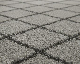 May include: Close-up of a gray carpet with a diamond pattern. The carpet has a soft, textured surface with dark gray lines forming the diamond grid. The neutral color palette makes it suitable for various interior designs.