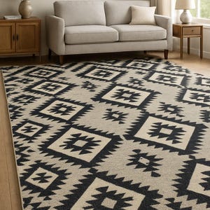May include: A large area rug with a geometric pattern in black and beige. The rug features repeating diamond shapes with a tribal-inspired design, adding a decorative element to the room. The rug is placed on a hardwood floor.