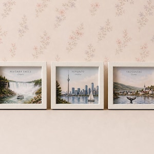 May include: Three framed prints with white frames. The prints depict scenic views of Niagara Falls, Toronto, and Tadoussac. Each print has text identifying the location. The background is a floral pattern.
