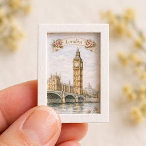 Peut inclure: Petite peinture à l'aquarelle de Big Ben et du Parlement de Londres, encadrée en blanc. L'œuvre représente un pont sur l'eau, avec le mot "London" sur une bannière. La peinture est tenue dans la main d'une personne.