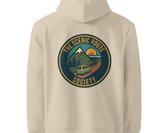 May include: A beige hooded sweatshirt with a circular graphic on the back. The graphic features a mountain, a road, a bus, and the text "THE SCENIC ROUTE SOCIETY" in a circular design. The sweatshirt has a drawstring hood and a kangaroo pocket.