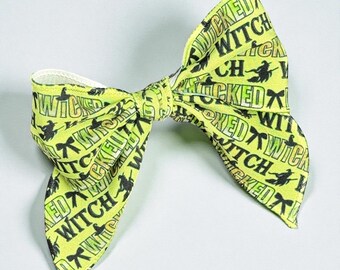 May include: A lime green bow with the words "WICKED WITCH" in black, along with a silhouette of a witch on a broom. The bow is tied in the center and has a white band on the inside.