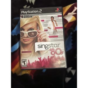 May include: A PlayStation 2 video game case for SingStar '80s. The cover features a woman wearing sunglasses and a man in a white suit. The game's title is in pink and white, with the ESRB rating for Teen.