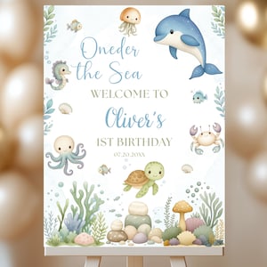 May include: A rectangular sign featuring watercolor illustrations of a dolphin, octopus, turtle, seahorse, jellyfish, and sea life. The text reads Oneder the Sea, WELCOME TO Oliver's 1ST BIRTHDAY, and 07.20.20XX, set against a white background with coral.