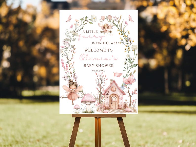 May include: A baby shower sign on a wooden easel. The sign features a fairy theme with floral accents, butterflies, and a fairy house. Text reads "A little fairy is on the way! Welcome to Olivia's Baby Shower 05.10.20XX."
