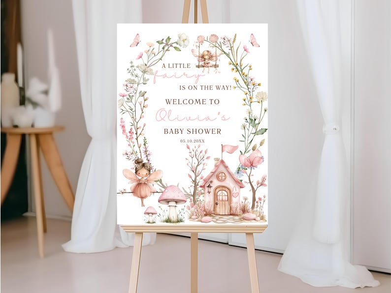 May include: A wooden easel displays a baby shower welcome sign. The sign features a watercolor illustration of a fairy theme, with a fairy house, mushrooms, and floral accents. Text reads "A little fairy is on the way! Welcome to Olivia's Baby Shower."