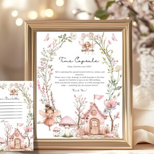 May include: A framed print and a card with a fairy theme. The print reads "Time Capsule" and includes text about capturing memories. The artwork features fairies, a pink house, mushrooms, and floral elements in soft pinks and greens.