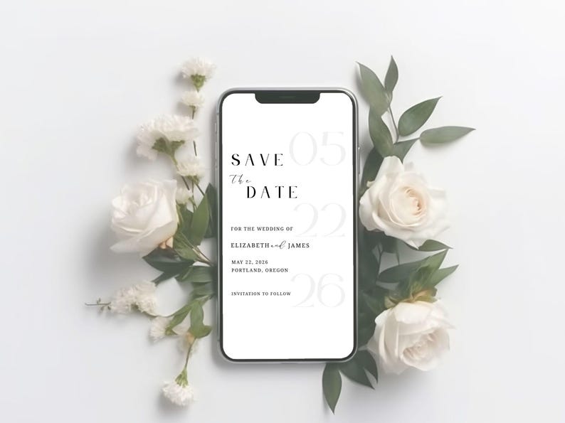 May include: A smartphone displays a wedding "Save the Date" announcement. The text includes the date, May 22, 2026, and the names Elizabeth and James, with the location Portland, Oregon. The phone is surrounded by white roses and greenery.
