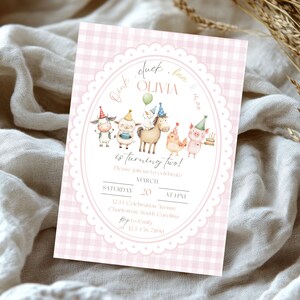 May include: A pink gingham-patterned invitation with an oval frame featuring cartoon farm animals. The text reads "Olivia is turning two!" with event details. The invitation is on a white fabric background.