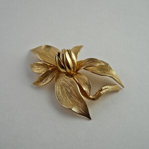 Puede incluir: Un broche dorado en forma de flor con cinco pétalos y un capullo central.
