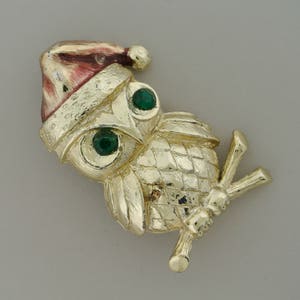 May include: Gold-tone owl brooch with green rhinestones for eyes and a red and gold Santa hat.