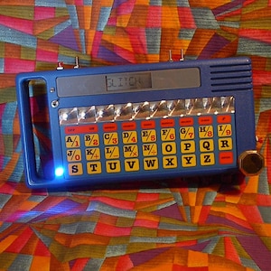 May include: A blue electronic device with a white display that reads "GLITON". The device has a keyboard with letters and numbers, and a row of lights above the keyboard.