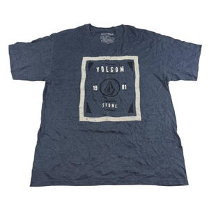May include: A navy blue t-shirt with a large square graphic on the front. The graphic features the word "VOLCOM" at the top, the numbers "19" and "91" on the sides, and the word "STONE" at the bottom. A diamond-shaped logo is in the center.