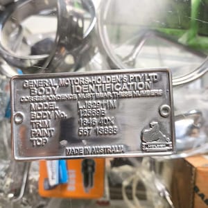 May include: A silver metal body identification plate from General Motors Holden's Pty Ltd. The plate includes the model, body number, trim, paint, and top details. The text "MADE IN AUSTRALIA" is also visible.