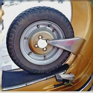 Peut inclure: Gros plan sur la roue de secours d'un scooter vintage montée sur le côté. Le pneu est noir avec une jante argentée et un centre doré. Un tuyau d'échappement chromé et d'autres détails chromés sont visibles sur la carrosserie du scooter.