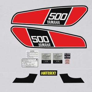 Puede incluir: Un conjunto de calcomanías rojas, negras y blancas para motocicletas Yamaha 500. Las calcomanías incluyen el logotipo de Yamaha, el número 500 y varias etiquetas y pegatinas de advertencia. También está presente el texto "HATESIX!".