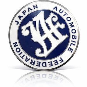 May include: A round, silver-edged emblem with a blue center. The words "JAPAN AUTOMOBILE FEDERATION" are in white around the edge. A stylized white "JAF" logo is in the center. The emblem is reflected below.