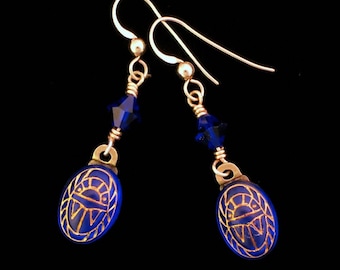 May include: Gold earrings with blue glass scarab beetle charms and blue crystal accents.
