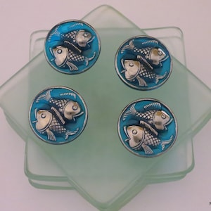 May include: Four blue glass coasters with silver fish designs. The coasters are stacked on top of each other.