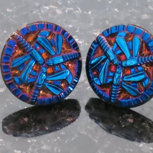 Op de afbeelding: Twee iriserende blauwe glazen knopen met een libellenmotief. De knopen hebben een iriserende afwerking in donkerblauw, paars en rood.