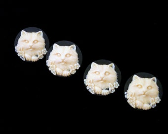 May include: Four white ceramic buttons with a raised design of a cat's face surrounded by flowers.