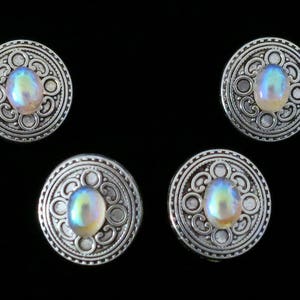 May include: Four silver-toned buttons with an iridescent center. Each button has a decorative design around the center.