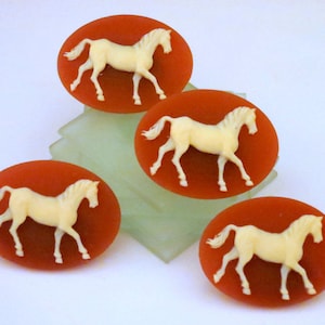 May include: Four oval-shaped, red-coloured, decorative, ceramic, horse figurines. Each figurine features a white horse with a raised design.