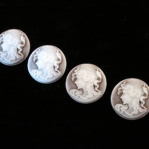 May include: Four white cameo buttons featuring a raised design of a woman's profile. The buttons are round and have a smooth, white surface.