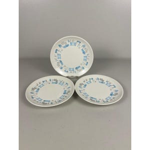 Op de afbeelding: Drie witte keramische borden met een blauw en grijs geometrisch patroon langs de rand. De borden zijn in een driehoekige formatie gerangschikt, waarbij hun ontwerp wordt getoond. De borden zijn waarschijnlijk bedoeld om voedsel op te dienen.