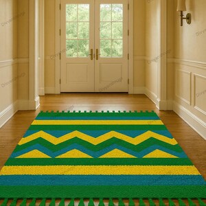 May include: A colorful area rug with a geometric pattern in shades of green, yellow, and blue. The rug features a zig-zag design and horizontal stripes, with tassels along the bottom edge. The rug is placed on a wooden floor.