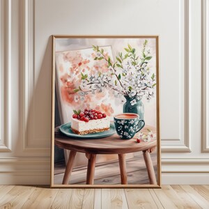 以下が含まれることがあります： ベリーがトッピングされたチーズケーキ、花柄のティーカップ、白い花の入った花瓶が描かれた、額入りの水彩画。 小さな木製のテーブルの上にシーンが設定されています。