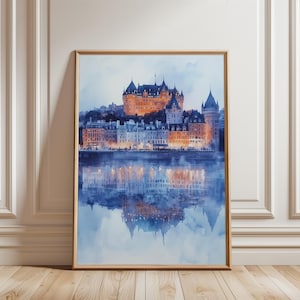 May include: Watercolour print of a cityscape featuring a castle and buildings along a waterfront. The artwork has warm orange and yellow lights against a cool blue sky and water, with reflections of the buildings below. The print is framed in a light brown wooden frame.