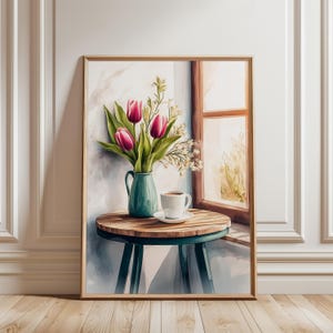 May include: A framed watercolor painting depicts a still life. A teal vase holds pink tulips and white flowers on a small wooden table with teal legs. A white coffee cup sits on a saucer. A window is in the background.