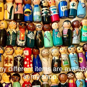 May include: A collection of hand-painted wooden peg dolls, each uniquely designed with different outfits and facial expressions. The dolls are painted in a variety of colors, including yellow, blue, green, and red. The text "Many different items are available in my shop" is visible.