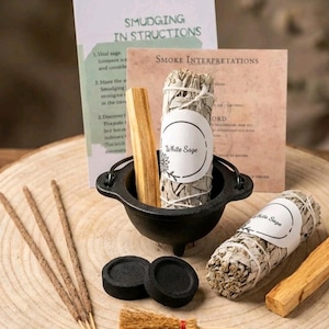 May include: A smudging kit featuring white sage, palo santo, and incense. The kit includes a small black cauldron, charcoal discs, and a miniature broom. Instructions are included. The items are arranged on a wooden surface.