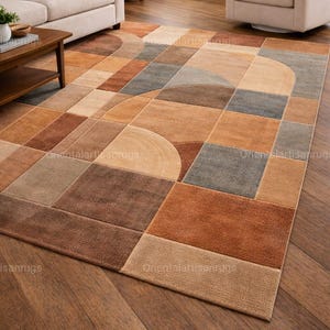 Op de afbeelding: Vloerkleed met geometrisch patroon in bruin-, beige- en grijstinten. Het vloerkleed heeft een modern design met vierkanten, rechthoeken en gebogen vormen. Het vloerkleed ligt op een parketvloer, in een woonkamer.