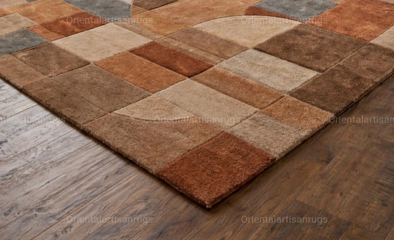 Op de afbeelding: Een geometrisch vloerkleed met een patchwork-ontwerp in bruin-, beige- en grijstinten. Het vloerkleed heeft een verscheidenheid aan rechthoekige en halfronde vormen, waardoor een gestructureerd oppervlak ontstaat. Het vloerkleed ligt op een donkere houten vloer.