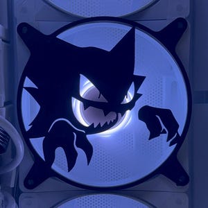 May include: A computer cooling system featuring three circular fans arranged vertically. The center fan is adorned with a black vinyl decal of a stylized creature with sharp teeth and pointed ears, illuminated by the bright white light of the fan.