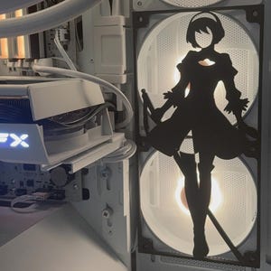 Könnte beinhalten: Innenraum eines weißen Computergehäuses mit beleuchteten Lüftern. Eine schwarze Silhouette einer Figur aus dem Spiel Nier: Automata ist über den Lüftern angebracht. Die Komponenten umfassen eine Grafikkarte und andere interne Hardware.
