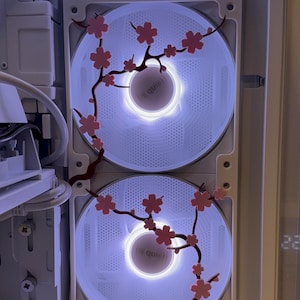 Puede incluir: Interior de una caja de ordenador con dos ventiladores blancos iluminados. Ramas decorativas de flores de cerezo rosas están fijadas a los ventiladores. Los ventiladores tienen un diseño circular con la palabra "quiet" visible en el centro.