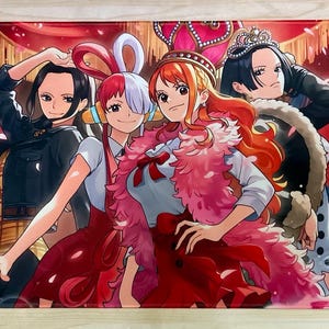 May include: A rectangular playmat featuring a vibrant anime-style illustration of four characters against a red curtain background. The characters have distinct hairstyles and outfits, including a pink feather boa, crowns, and various colorful accessories.